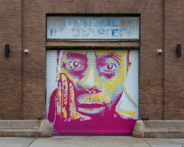 Mural of James Baldwin's face painted in pink and yellow on a garage door.