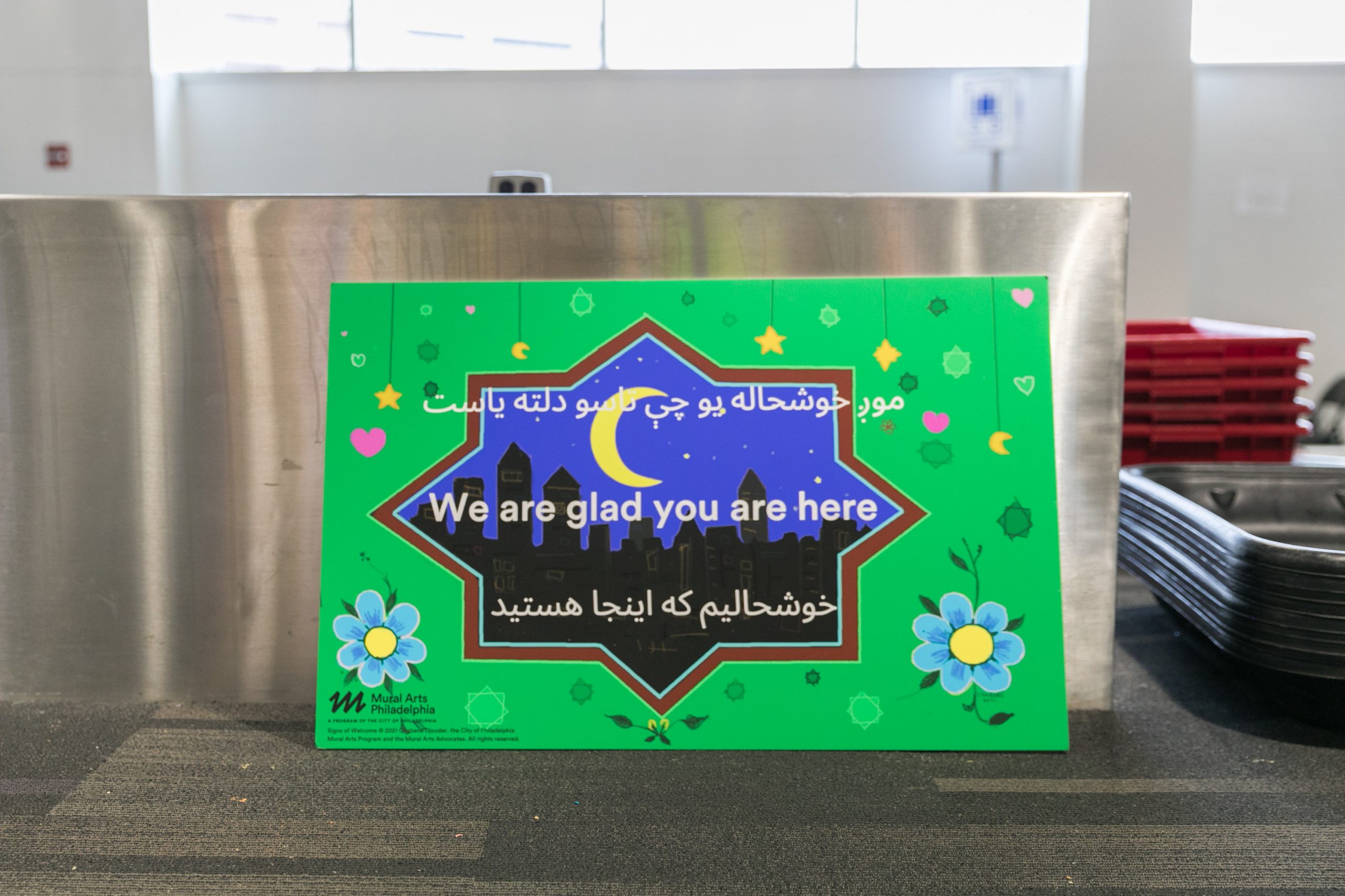 A green sign decorated with flowers and featuring a drawing of a city skyline at night says, 
